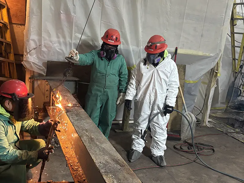 Three certified asbestos remediation specialists in protective gear welding beam