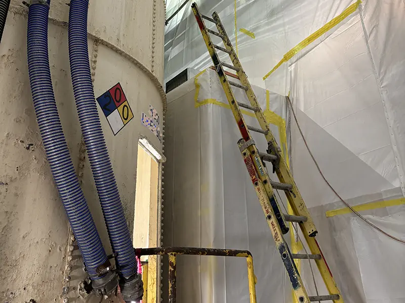 ladder leaning against a large piece of equipment with walls that are sheeted for lead abatement